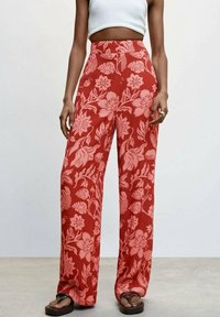 Rote, blumige weite Hosen mit pinken Motiven, hoher Taillenschnitt und leichtem Stoff. Dazu einfache schwarze Sandalen.