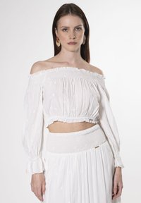 Weißes schulterfreies Crop-Top mit langen Ärmeln, das mit Rüschendetails und floraler Stickerei verziert ist, kombiniert mit einem passenden Rüschensrock.