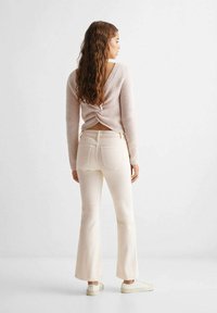 Maglione a coste color rosa chiaro con dettagli sulla schiena torcigliati, abbinato a jeans flare color bianco sporco e sneakers bianche, visto da dietro.