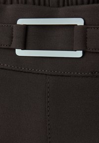 Brun tygbälte med ett rektangulärt silvermetallspänne, med slät textur och sömdetaljer på varje sida av spännet.