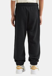 Pantaloni della tuta neri con cintura elastica e polsini alle caviglie, realizzati in tessuto morbido; indossati con sneaker bianche con accenti gialli.