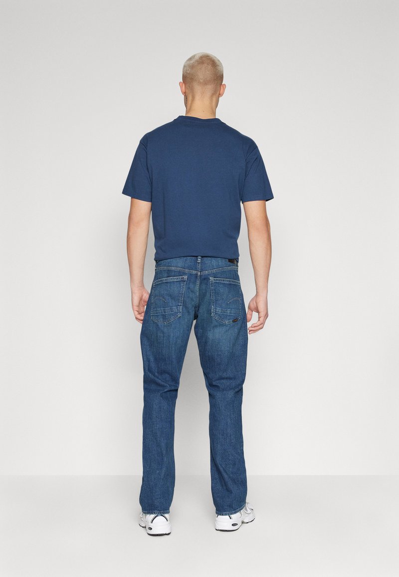 T-shirt en coton bleu marine et jeans en denim bleu, tous deux à coupe décontractée. Le T-shirt présente un col arrondi ; les jeans ont des poches arrière.