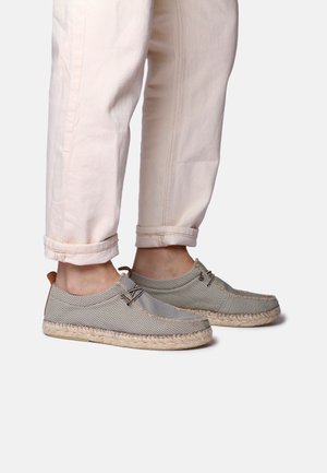 Gray mesh espadrilles with a braided jute sole, featuring brown leather accents and laces, worn with rolled light-colored trousers.