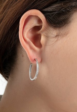 Silver hoop earring with an open design, featuring a row of small clear stones along one edge, highlighting its reflective surface.