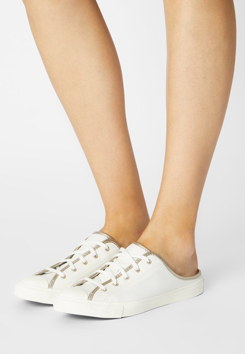 Sneaker bianche in tela con accenti dorati, design slip-on, allacciatura frontale, punta rotonda e suola di gomma testurizzata.