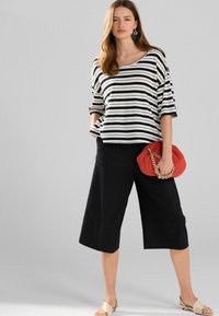 Black and white striped top, wide black culottes, and a red clutch with a chain. Model wears beige sandals and statement earrings.
