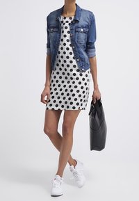 Chaqueta de denim con detalles de botones, sobre un vestido blanco con lunares negros. Zapatillas blancas y un bolso tote negro completan el look.