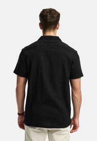 Short-sleeve black shirt with a relaxed fit, soft fabric texture, and a classic collar. Features a straight hem and rolled sleeves.