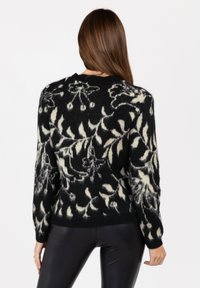 Schwarzer und cremefarbener Pullover mit Blumenmuster, gefertigt aus weichem, strukturiertem Stoff, mit langen Ärmeln und einem runden Ausschnitt.