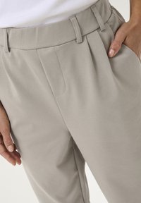 Pantalons adaptés beige clair en tissu doux, dotés d'une taille haute, de plis avant et de poches latérales dissimulées.