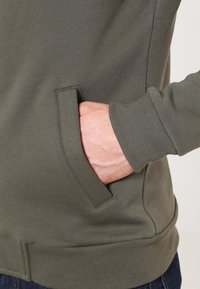 Olive green sweatshirt with a fitted silhouette, ribbed cuffs, and a side pocket. Made from soft, textured cotton blend fabric.