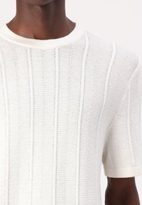 Kurzarmpullover aus Wolle in Weiß mit geripptem Muster und horizontalen Streifen. Der runde Halsausschnitt und die weichen Bündchen runden das Design ab.