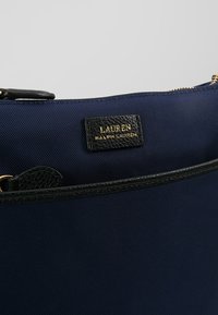 Borsa in tessuto blu navy con rifiniture in pelle nera, dotata di un'etichetta in oro con la scritta "LAUREN RALPH LAUREN" sopra una chiusura con zip.