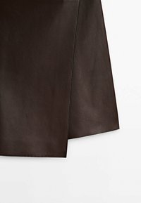 Jupe en cuir marron foncé avec des coutures nettes, montrant un détail de fente frontale sur fond blanc.