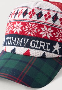 Gorro de punto con la parte superior de patrón rojo, blanco y azul marino que presenta copos de nieve; visera de cuadros verdes; "TOMMY GIRL" bordado en blanco en la parte frontal.