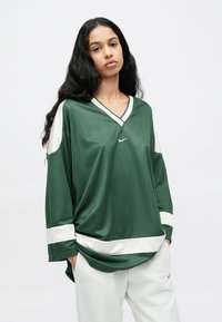 Πράσινο αθλητικό τοπ με μακριά μανίκια και ρίγες, με λευκές λεπτομέρειες, λαιμόκοψη σε σχήμα V και άνετη εφαρμογή. Διαθέτει μικρό λογότυπο Nike στο μπροστινό μέρος.