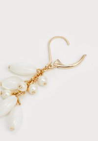 Boucles d'oreilles pendantes en doré ornées de plusieurs perles blanches en forme d'ovale et de petites perles rondes, attachées par une chaîne avec un fermoir à ressort.