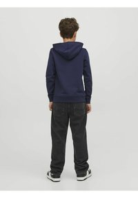 Sudadera azul marino con capucha ajustable, puños de canalé y corte recto, combinada con un pantalón vaquero gris oscuro de corte holgado y zapatillas negras.