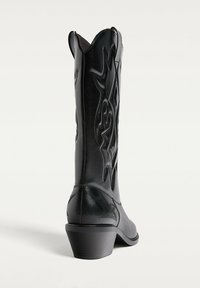 Black leather cowboy boot with stitched flame patterns, mid-height stacked heel, and scalloped top edge, shown angled from back and side.