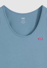 Débardeur bleu en coton avec un col rond, doté d'une petite étiquette logo rouge Levi's sur le côté gauche. Texture lisse et design simple.