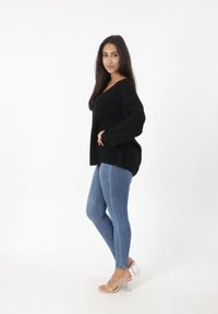 Czarny, oversize sweter z dzianiny połączony z niebieskimi rurkami i przezroczystymi sandałami na wysokim obcasie. Gładka faktura i luźny krój.