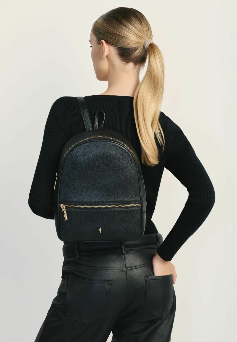 Czarny skórzany plecak o zaokrąglonym kształcie, z przednią kieszenią na zamek i złotymi akcentami. Noszony na plecach z regulowanymi paskami.