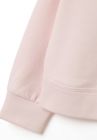 Tejido de sudadera rosa claro con una textura suave, con puños y costuras acanaladas, que presenta un diseño minimalista.