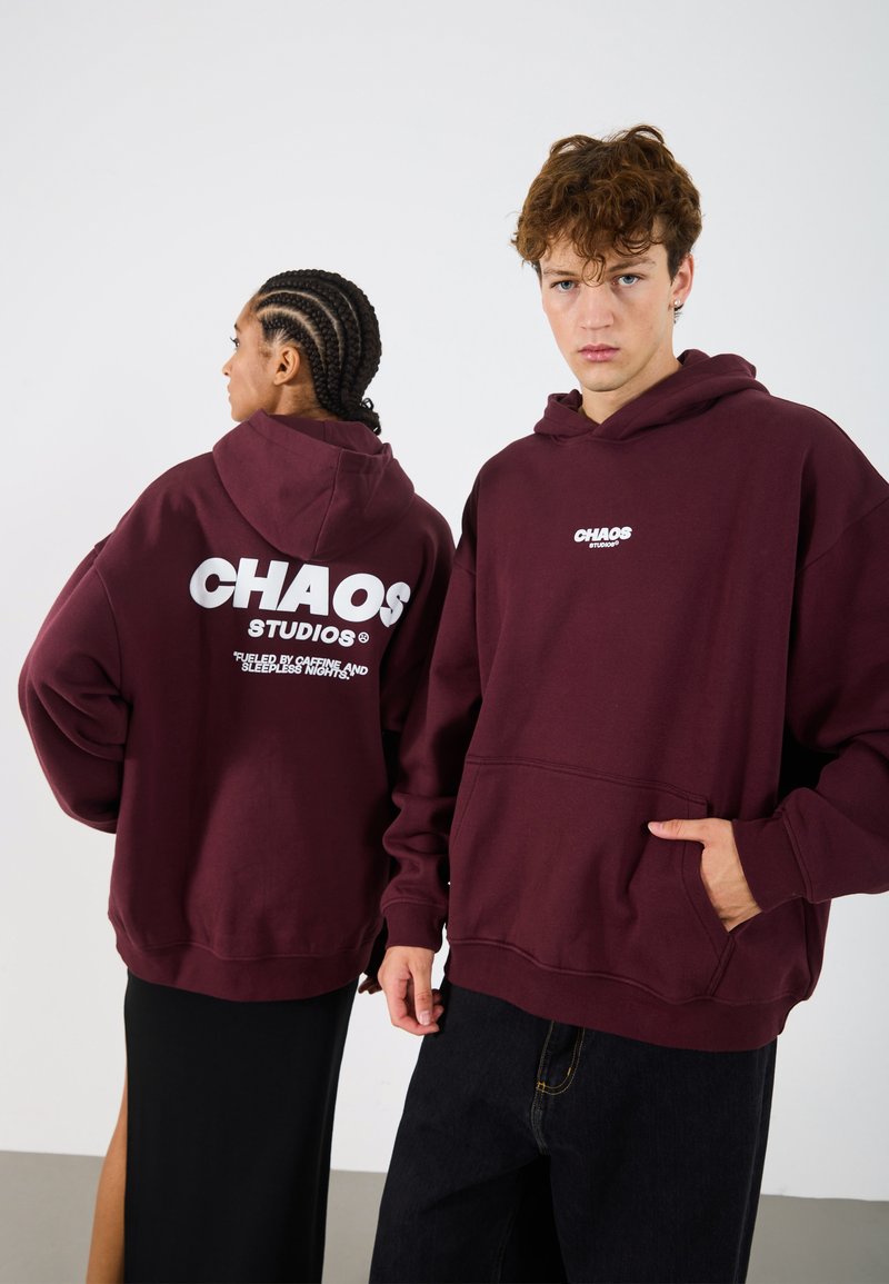 Hanorace bordeaux cu buzunare tip cangur în față. Logo-uri mari albe "CHAOS STUDIOS" pe spate și pe piept. Material din bumbac, croială supradimensionată, design casual.
