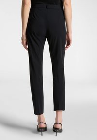 Pantaloni neri su misura realizzati in un tessuto morbido e leggero. Vestibilità slim con vita media e gamba corta, abbinati a eleganti tacchi a spillo.