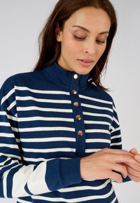 Pullover a righe blu scuro e bianche con un alto collo, chiusura a bottoni a pressione e maniche bianche a contrasto. Tessuto morbido.