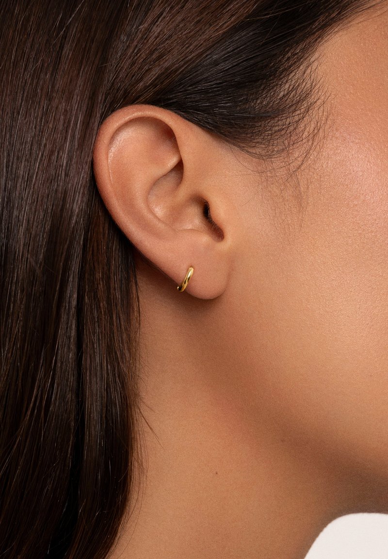 Orecchino in oro a cerchio adagiato su un orecchio forato, presenta una finitura liscia e lucida con un design semplice e arrotondato.