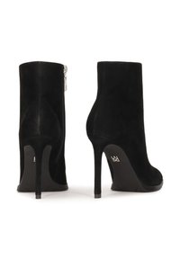 Botas de tobillo de ante negro con una silueta elegante, tacón alto y detalle de cremallera lateral. Textura suave, diseño acampanado y punta redonda.