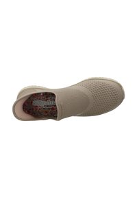 Zapato slip-on de un ligero tono beige, con material de malla, superficie texturizada y plantilla con un patrón floral. Presenta una suela acolchada y flexible.