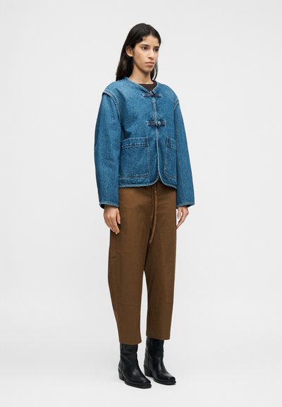 Τζιν μπουφάν με στρογγυλή λαιμόκοψη, δύο τσέπες μπροστά και κλείσιμο με κουμπιά toggle. Συνδυάζεται με καφέ άνετο παντελόνι και μαύρα μποτάκια αστραγάλου.