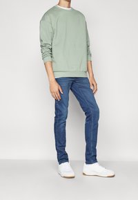 Ljusgrön sweatshirt med rund hals, tillsammans med mörkblå slim-fit jeans. Skotillbehör inkluderar vita sneakers med gummisulor.
