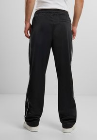 Pantaloni sportivi negri dintr-o țesătură netedă, cu o croială lejeră, talie elastică și dungi albe pe laterale pentru contrast.