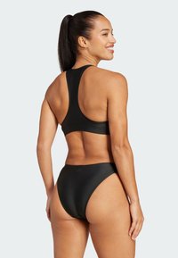 Bikini sportivo nero con top a schiena scoperta. Il materiale è liscio, evidenziando una vestibilità slim. Presenta un design minimalista e bordi senza cuciture.