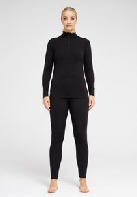 Sort termisk top med høj hals og lynlås, parret med matchende sorte leggings. Begge er lavet af et blødt og strækbart materiale for komfort.