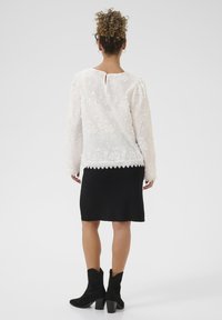 Blusa floreale bianca con maniche lunghe, bordi in pizzo e schiena a apertura a chiave, abbinata a una gonna nera aderente e stivaletti neri.