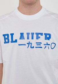 T-shirt bianca in cotone con stampa blu che riporta la scritta "BLAUER" e caratteri giapponesi, con collo rotondo e maniche corte.