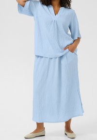 Ensemble deux pièces bleu clair texturé comprenant un haut à manches courtes avec un col en V et une longue jupe fluide avec des poches latérales.