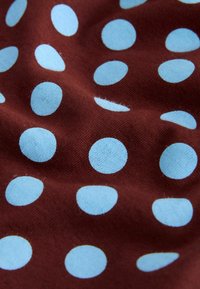 Tissu marron avec un motif de pois bleu clair espacés régulièrement, présentant une texture visible et des plis.