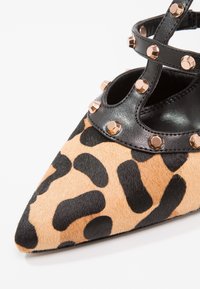 Chaussure à bout pointu imprimé léopard avec des brides en cuir noir ornées de clous métalliques ronds couleur or.