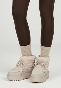 Lys beige, bløde ankelstøvler med polstret design, gummisål og snøredetalje; parret med ribbet strikkede cremede sokker.