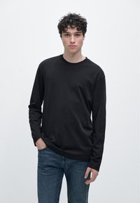 Svart bomulls-t-shirt med långärmar och rund halsringning, avslappnad passform och minimalistisk design, bärs med jeans.