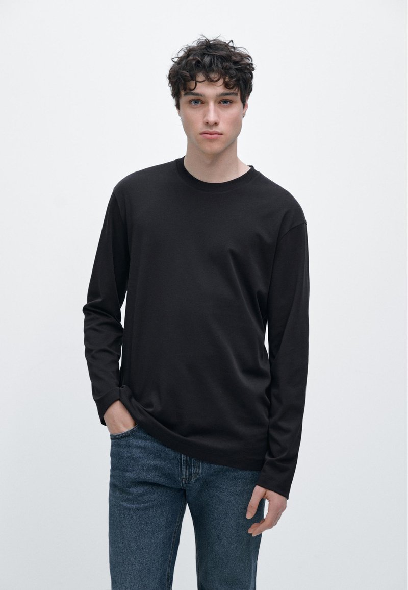 Svart bomulls-t-shirt med långärmar och rund halsringning, avslappnad passform och minimalistisk design, bärs med jeans.