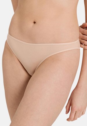 Gros plan d'une personne portant un sous-vêtement beige sans coutures, montrant le bas de l'abdomen et le haut des cuisses avec une main reposant sur la hanche.