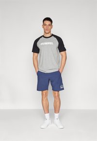 Gray and black short-sleeved t-shirt with "HUMMEL" logo, paired with blue shorts featuring white logo. White sneakers and ankle socks.