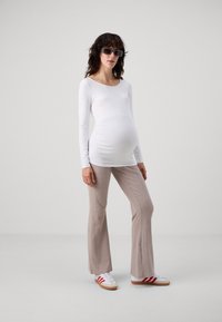 White long-sleeve top, ribbed pale beige flared pants, and white sneakers with red stripes. Model has a visible pregnant belly and sunglasses.