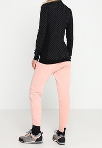 Musta pitkähihainen paita timanttikuvioilla, yhdistetty vaaleanpunaisiin collegehousuihin. Jalkineissa on harmaat yksityiskohdat ja teksturoitu muotoilu.